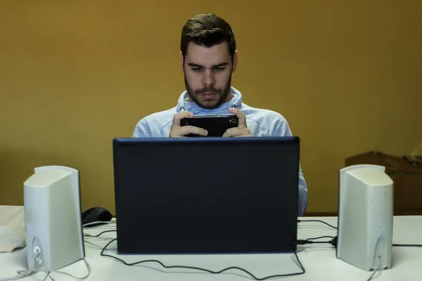 Genç adam cep telefonunu kullanarak tablet, dizüstü bilgisayar ve kulaklıklar