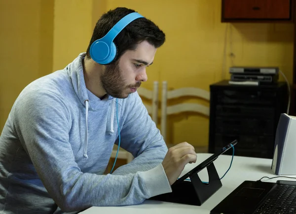 Genç adam cep telefonunu kullanarak tablet, dizüstü bilgisayar ve kulaklıklar