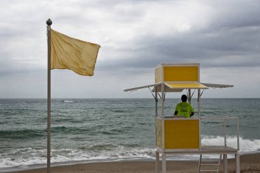 Sarı uyarı bayrağı ile bir plajda izlerken bir cankurtaran kulesinde Cankurtaran.