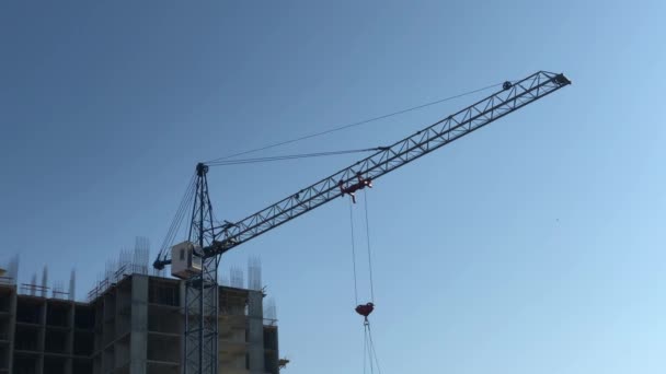 Grúa de construcción gira la flecha sobre el fondo de la construcción y el cielo — Vídeos de Stock