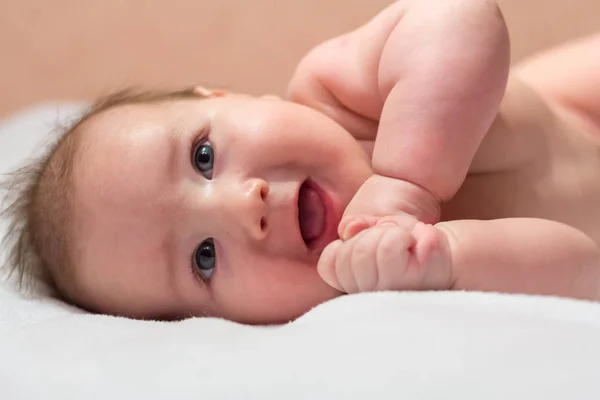 Bebê recém-nascido deitado de lado e sorrindo em um lençol branco e olhando para cima — Fotografia de Stock