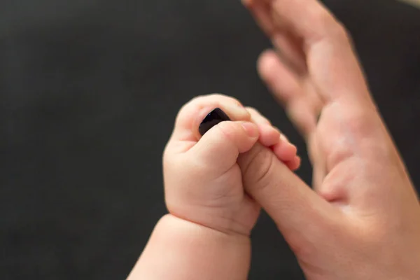 Kids hand holds the finger of his moms hand on a black background — Stock Photo, Image