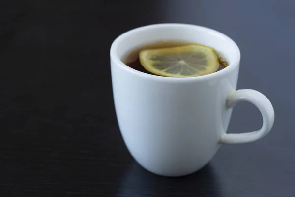 Té con limón en una taza blanca y una tetera blanca sobre un fondo oscuro — Foto de Stock