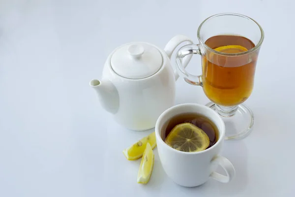 Чай с лимоном в белой и стеклянной чашке и белый чайник на белом фоне — стоковое фото