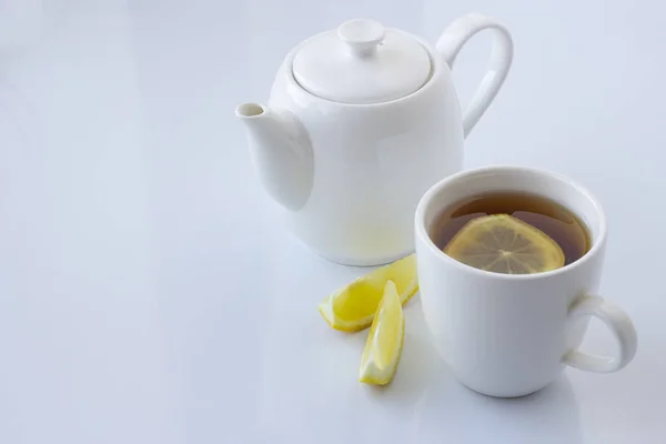 Tea with lemon in a white cup and a white teapot on a white background — Stock Photo, Image