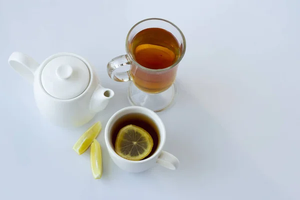 Tea with lemon in a white and glass cup and a white teapot on a white background — Stock Photo, Image