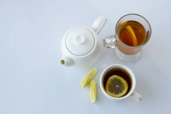 Tea with lemon in a white and glass cup and a white teapot on a white background — Stock Photo, Image