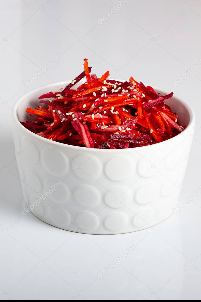 Vegetable salad of apple, carrot and beetroot with lemon juice, sesame seeds and vegetable oil in a white deep plate