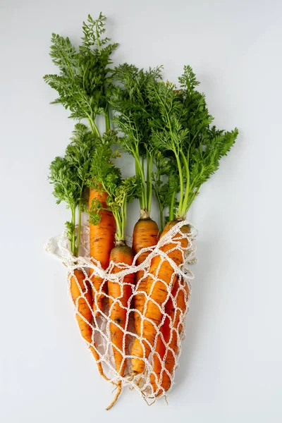 Two Fresh raw carrots with tops in an eco bag close-up on a white background