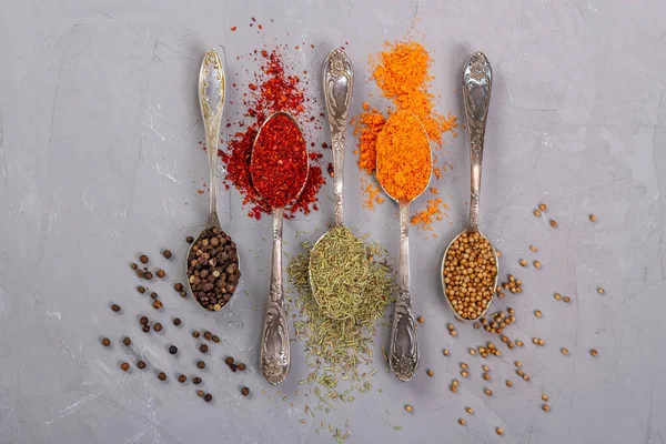 Zerdeçal tozu, paprika, kişniş ve gri arka planda metal çay kaşıklarıyla siyah biber.