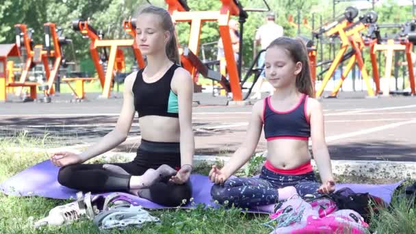 スポーツウェアを着た2人の女の子がスポーツ界で屋外で瞑想しています 高品質のフルHd映像 — ストック動画
