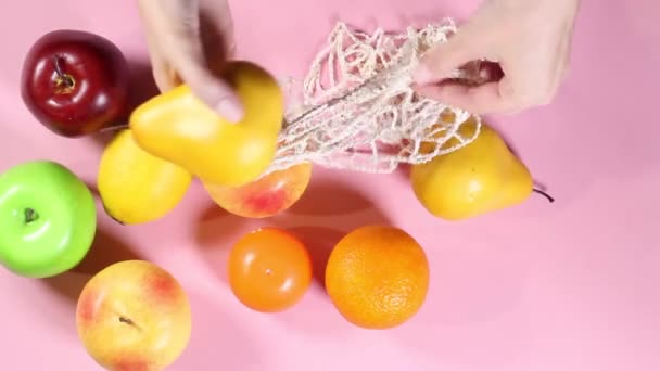 Vrouwelijke Handen Stapelen Vruchten Een Touwtje Zak Een Roze Achtergrond — Stockvideo