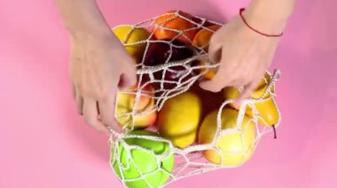 Kadın eli örgü bir alışveriş çantasından meyve alır.