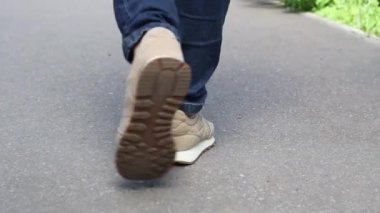 Bej spor ayakkabılı ve mavi kotlu bacaklar asfalt yolda yavaşlar. Yüksek kaliteli FullHD görüntüler