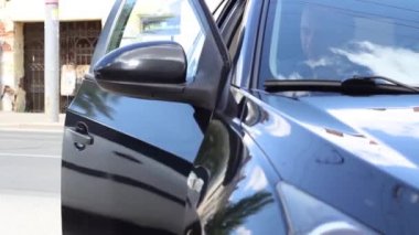 Mavi kısa kollu beyaz bir adam siyah bir arabadan iniyor.