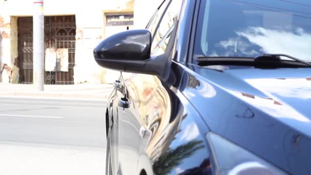 Fiatal fehér férfi kék rövid ujjú pólóban beszáll egy fekete autóba. — Stock videók
