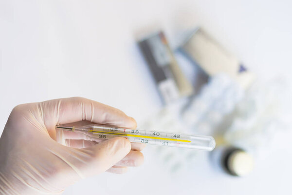 Hand in medical glove holding a thermometer with pills and medications