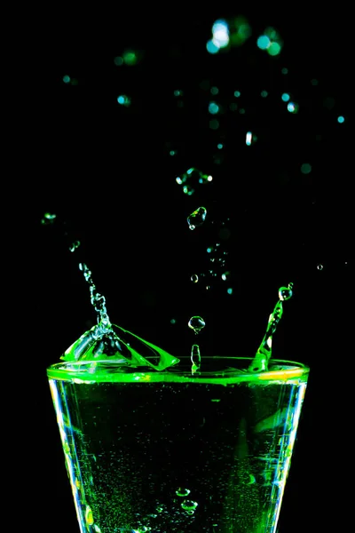 Cocktail beverage drink green splashes close-up. Glass and drops abstract black background