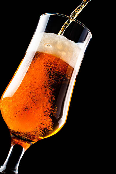 Beer is pouring into a glass from bottle isolated on black background