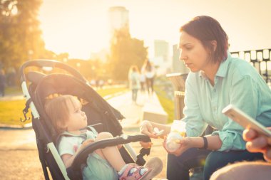 Genç anne, bebek arabasındaki küçük kızı besler.
