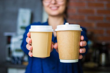 genç gülümseyen barista kız logosu için yer ile gitmek için kahve bir kağıt bardak ile ellerini tutar