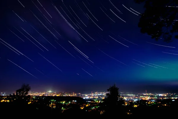 Звездные тропы в ясном ночном небе над городом с многочисленными огнями вид с горы — стоковое фото