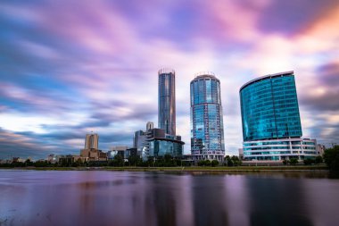 Güzel geniş açı uzun pozlama cityscape Yekaterinburg şehir, Bulanık mavi ve mor bulutlar ile gün batımında Rusya. Iset Nehri'nin suyuna yansıyan gökdelenler