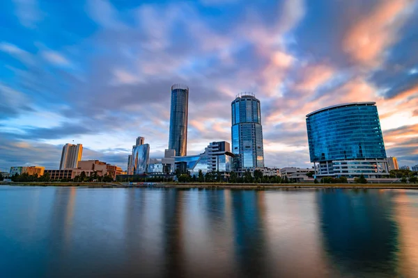 Güzel geniş açı uzun pozlama cityscape Yekaterinburg şehir, Bulanık mavi ve mor bulutlar ile gün batımında Rusya. Iset Nehri'nin suyuna yansıyan gökdelenler