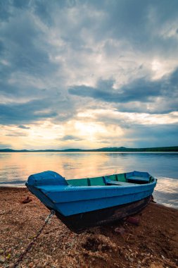 Mavi tekne gün batımında bulutlu gökyüzü altında göl kıyısında demirlemiş
