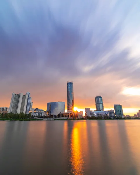 Hermosa puesta de sol nublado en el estanque de la ciudad. Paisaje urbano de larga exposición de Ekaterimburgo, Rusia con rascacielos reflejándose en el agua — Foto de Stock