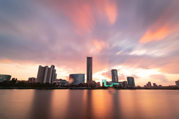 Hermosa puesta de sol nublado en el estanque de la ciudad. Paisaje urbano de larga exposición de Ekaterimburgo, Rusia con rascacielos reflejándose en el agua — Foto de Stock