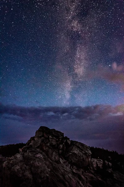 Galaxia de la Vía Láctea en el cielo nocturno sobre montañas rocosas y nubes tormentosas Imagen De Stock