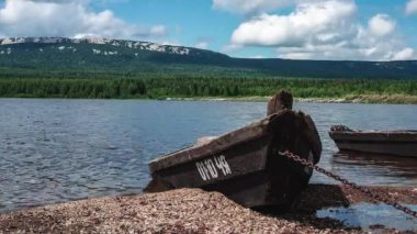Dağ gölünün üzerinde hareket eden bulutlar ve kıyıya demir atmış bir tekne 4K sürat videosu.