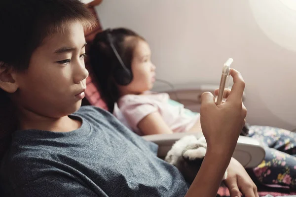 Asian kids using smart phone in flight, family traveling abroad with children
