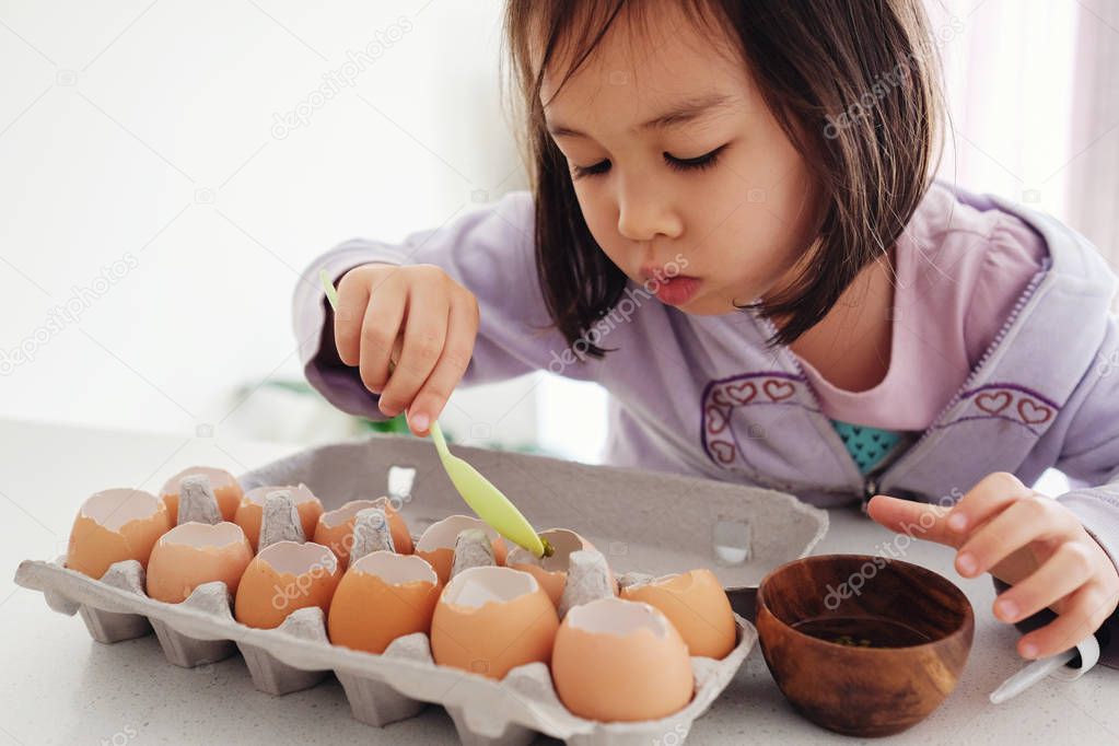 Mixed Asian girl planting seeds into eggshells, eco gardening,  montessori, education, reuse concept
