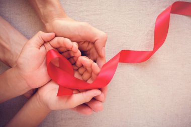 Yetişkin ve Çocuk ellerini tutarak kırmızı kurdele, HIV farkındalık kavramı, Dünya AIDS Günü
