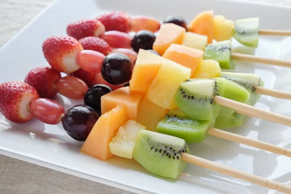 fresh rainbow fruits skewers on white plate