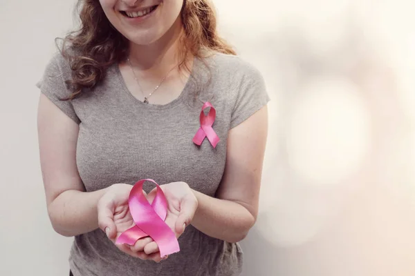 woman  holding pink ribbon in hands, breast cancer awareness and October pink concept