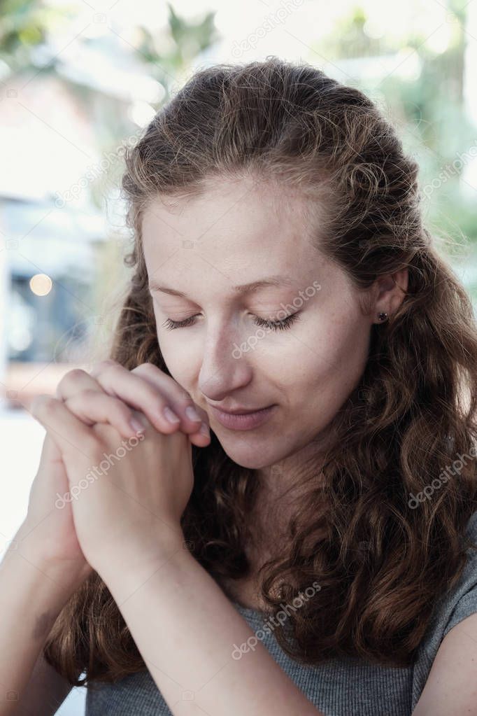 Young woman praying with closed eyes outdoor 