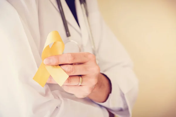 黄色いゴールド リボン 肉腫の意識 小児癌意識を保持している医師の手 — ストック写真