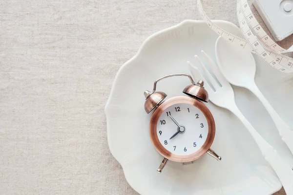 A clock, spoon and fork on a plate