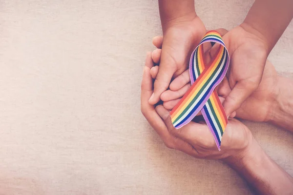 Mãos segurando gay orgulho arco-íris fita para LGBT consciência — Fotografia de Stock