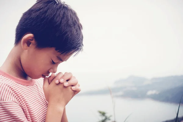 Мультикультурний азіатський хлопчик молиться з закритими руками в горах — стокове фото