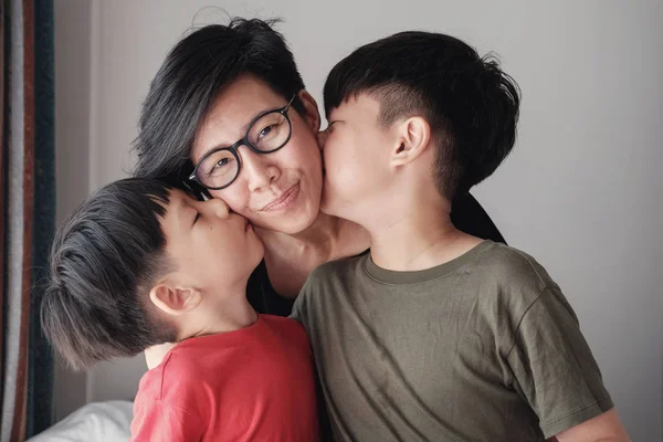 Two sons kissing their mother at home, Happy Asian family portra