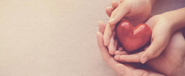 Manos adultas y del niño ahuecando el corazón rojo, la salud del corazón y donat — Foto de Stock