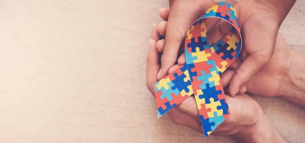 Mãos segurando fita de quebra-cabeça para banner consciência autismo — Fotografia de Stock