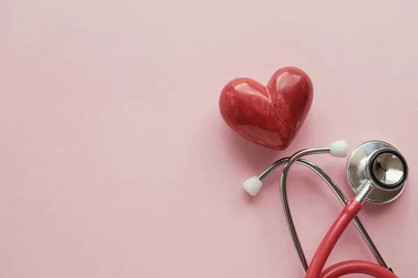 Corazón rojo con estetoscopio sobre fondo rosa, salud del corazón, él — Foto de Stock