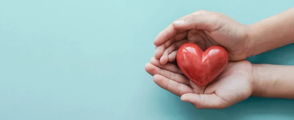 Manos sosteniendo el corazón rojo sobre fondo azul, cuidado de la salud, amor, o — Foto de Stock