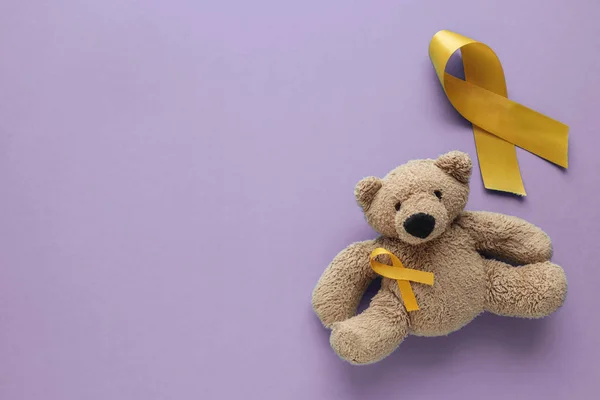 Children soft toy brown bear with yellow gold ribbons on purple — Stock Photo, Image
