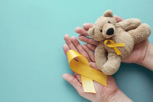 Ręce trzymanie dzieci miękkie zabawka brązowy niedźwiedź z żółtym złotem ribb — Zdjęcie stockowe